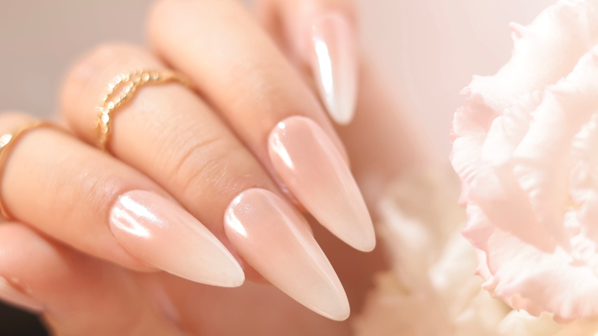 Glossy pearly nude almond nails beside a soft pink flower