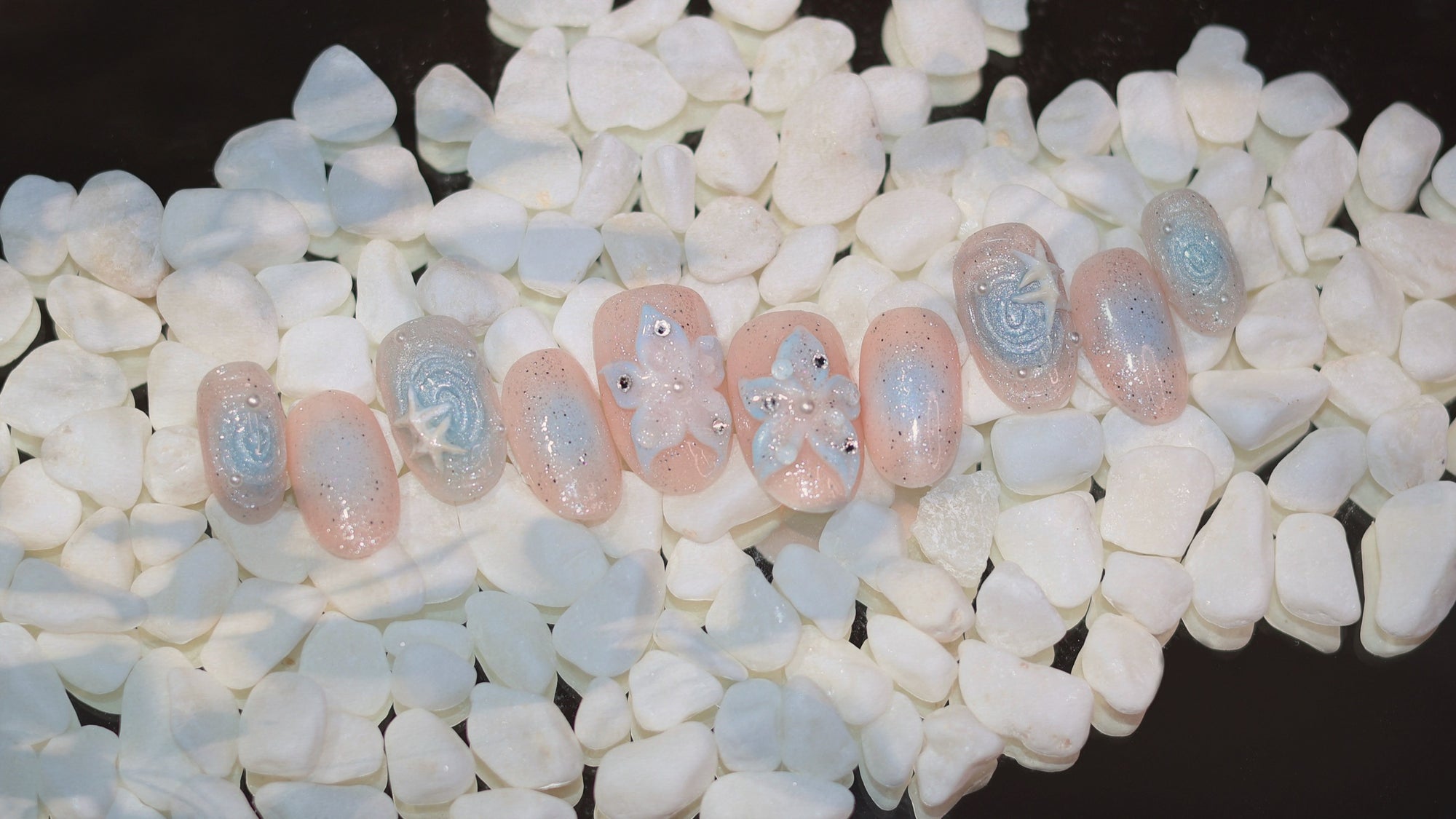 Stardust press-on set on white pebbles — homepage hero